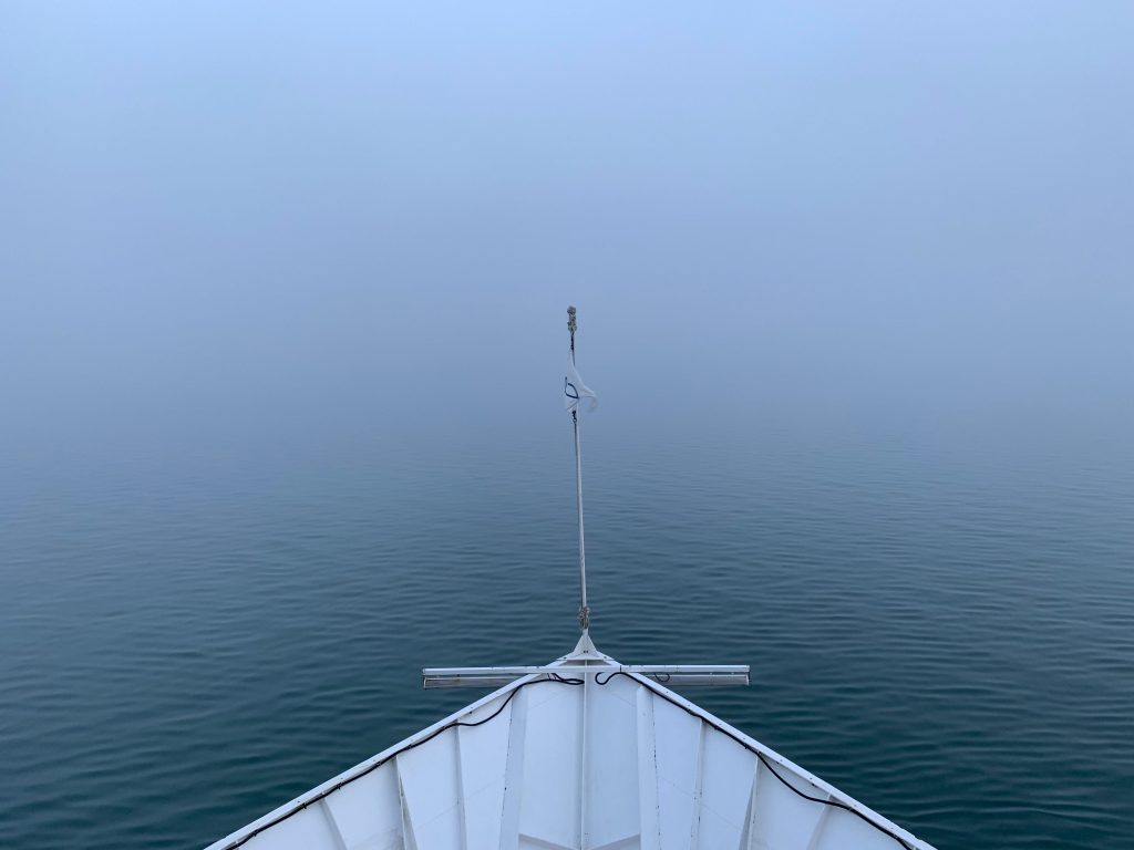 Very foggy view of Alaska with the bow of the Wilderness Discoverer ship at the bottom of the photo.